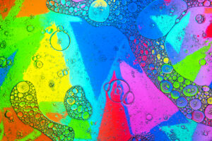 Ansammlungen von Seifenblasen, die auf dem Wasser vor einem mehrfarbigen abstrakten Hintergrund mit leuchtenden Dreiecken schweben.