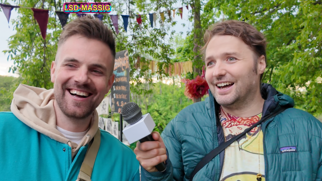 Nicolai Binner und Simon Ruane lachen bei einem Interview auf der TRYP Expo, darüber der Schriftzug „LSD-MÄSSIG“.